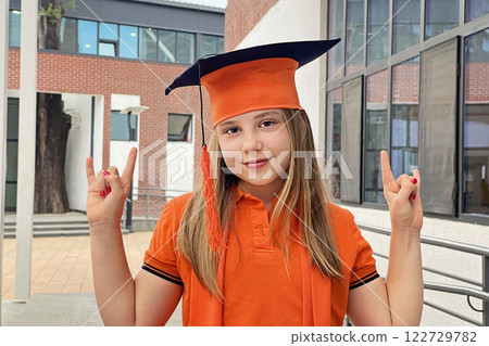Schoolgirl is wearing a graduation cap having fun. Child student in school yard portrait 122729782