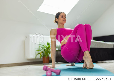 Cute sporty woman in pink leggings doing yoga exercises in a bright room 122730303