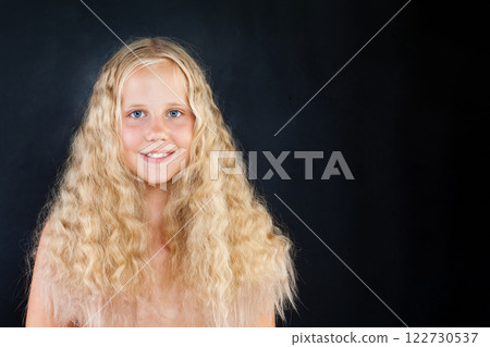Healthy child with blond long wavy hair looking at camera on black background, fashion portrait 122730537