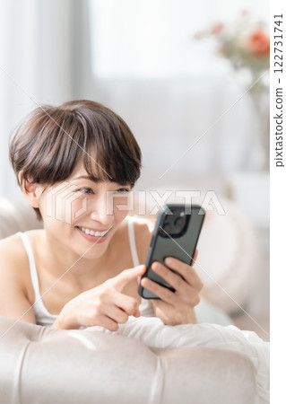 一位中年婦女一邊微笑一邊看著她的智慧型手機 一位中年婦女一邊微笑一邊看著她的智慧型手機 122731741
