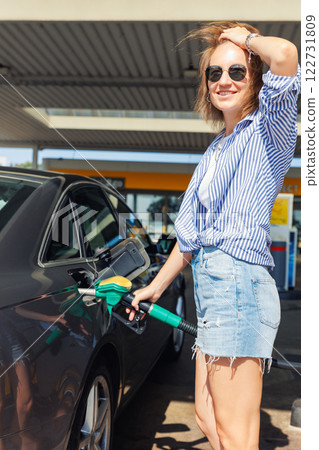 Portrait happy smiling woman sunglasses casual outfit refuel car gas station sunny summer day. Confident female person filling auto tank fuel holding fuel nozzle enjoy travel vacation journey trip 122731809