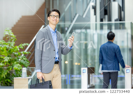 Businessman holding a smartphone in front of the ticket gate Businessman holding a smartphone in front of the ticket gate 122733440