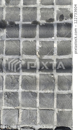 An image features textured gray cobblestone pavement with grid pattern, showcasing unique surface details and shadows 122733604