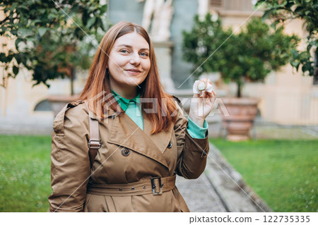 Happy 30s woman holding Sicilian cannolo tube pastry filled with cream outdoors. Travel, Italy, food and holidays concept. Young woman eating traditional delicious cake cannoli, Traveling Europe 122735335