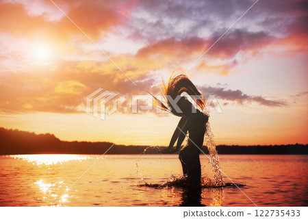 Young, beautiful girl walking at the beach at sunset. Stylish woman with long hair standing in blouse and jeans shorts 122735433
