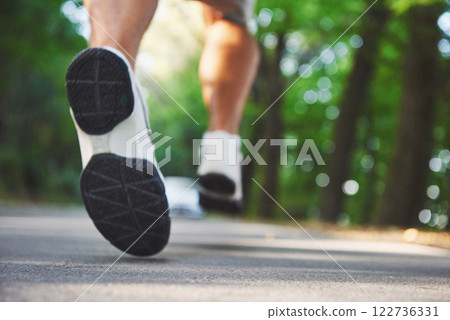 Outdoor cross-country running in concept for exercising, fitness and healthy lifestyle. Close up of feet of young runner man running along road in the park Outdoor cross-country running in concept for exercising, fitness and healthy lifestyle. Close up of feet of young runner man running along road in the park 122736331