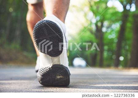 Outdoor cross-country running in concept for exercising, fitness and healthy lifestyle. Close up of feet of young runner man running along road in the park 122736336