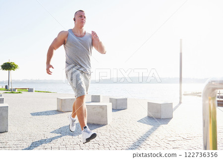 man runner doing stretching exercise, preparing for morning workout in the park 122736356
