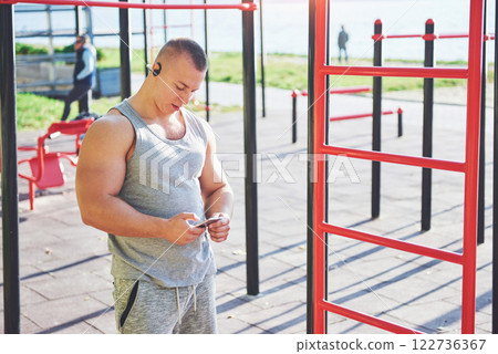 Muscular man with beautiful torso exercising on horizontal bars on a blurred park background. Young man doing pull-ups outdoors Muscular man with beautiful torso exercising on horizontal bars on a blurred park background. Young man doing pull-ups outdoors 122736367