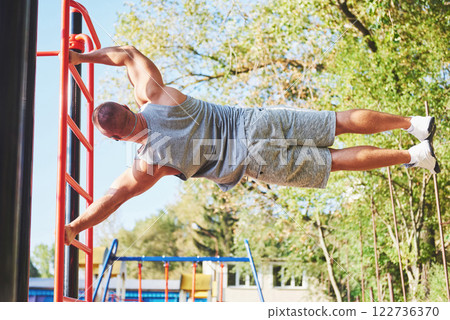 Muscular man with beautiful torso exercising on horizontal bars on a blurred park background. Young man doing pull-ups outdoors 122736370