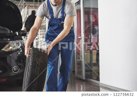 Technician with a blue workwear, holding a wrench and a tire while showing thumb up 122736632