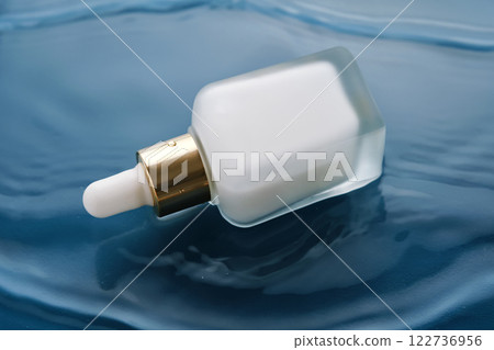 Bottle with white moisturizing serum in water on blue background. 122736956