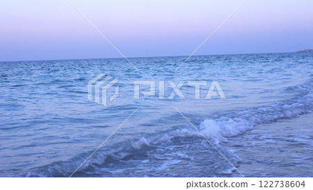 Ocean waves with soft white crests meet sandy shore under sky tinged with pre-dawn hues, creating tranquil scene evoking peace before sun rises. Morning calm concept. 122738604