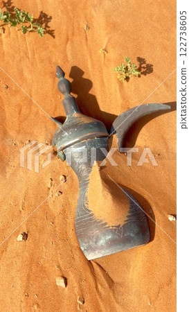 Desert coffee pot rests on grains of sunlit sand, preserving cultural heritage. This pot connects generations through coffee traditions in desert communities and history Arabic Dallah, pot 122738605