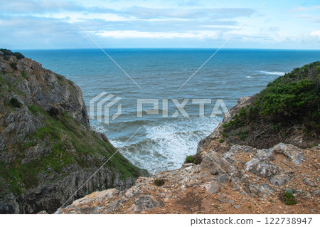 Panorama of the ocean coast and rock bay, Atlantic Ocean in winter, stormy sea waves with white lambs roll ashore with sheer rocks, beautiful cloudscape, dramatic landscape, gloomy seascape Panorama of the ocean coast and rock bay, Atlantic Ocean in winter, stormy sea waves with white lambs roll ashore with sheer rocks, beautiful cloudscape, dramatic landscape, gloomy seascape 122738947