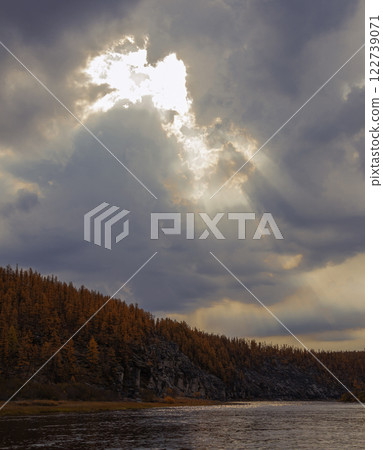 Cloudy and watery landscape with rays of sunlight over the autumn taiga river. Cloudy and watery landscape with rays of sunlight over the autumn taiga river. 122739071