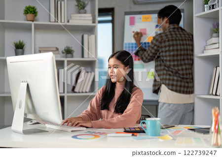 Creative designer focused on digital work while collaborative teammate organizes ideas on a mood board Creative designer focused on digital work while collaborative teammate organizes ideas on a mood board 122739247