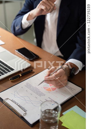 Senior financial analyst preparing report with charts and graphs in professional office setting 122739289