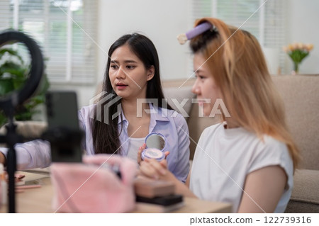 Beauty broker discussing makeup techniques with a friend during a live broadcast, showcasing collaboration and beauty tips. 122739316