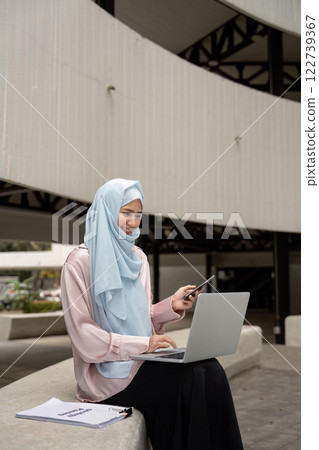 Muslim woman in hijab multitasking with laptop and smartphone for business Muslim woman in hijab multitasking with laptop and smartphone for business 122739367