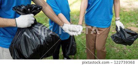 Connected family volunteers holding hands while collecting garbage in a park, symbolizing unity and environmental responsibility. 122739368