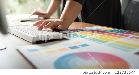 Graphic designer working on a computer keyboard with color charts at a creative desk. Graphic designer working on a computer keyboard with color charts at a creative desk. 122739544