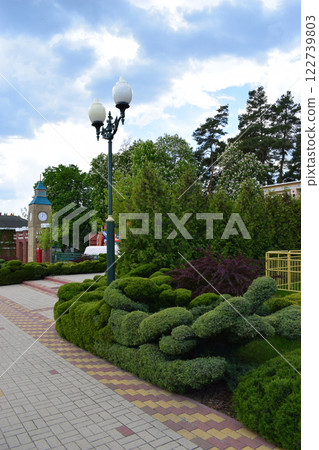 Kharkov, Ukraine, 14 May 2024. A landscaped garden scene featuring neatly trimmed greenery and decorative shrubs along a paved path. European Clock Tower Garden Kharkov, Ukraine, 14 May 2024. A landscaped garden scene featuring neatly trimmed greenery and decorative shrubs along a paved path. European Clock Tower Garden 122739803