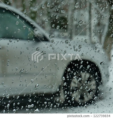 A blurred car parked in the yard is visible through the drops on the car glass A blurred car parked in the yard is visible through the drops on the car glass 122739834