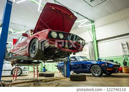 In a fully equipped automotive workshop environment, there are two classic cars being carefully serviced 122740118