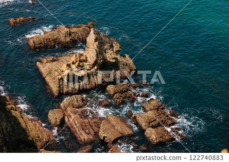 Jagged rock formations emerging from the deep blue sea with waves Jagged rock formations emerging from the deep blue sea with waves 122740883