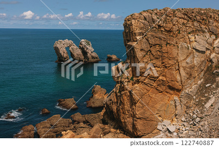 Massive coastal cliffs with a striking rock arch emerging from the deep blue sea 122740887