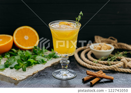 Refreshing citrus cocktail with orange slices, cinnamon and herbs in glass on dark background 122741050