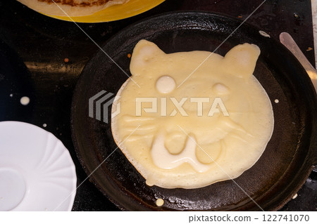 Creative pancake in a pan resembling a bear face, with eyes, nose, and smiling mouth. 122741070