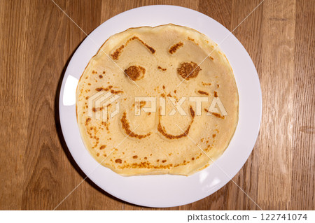 The image shows a delightful pancake cooked on the white plate, featuring a playful face with eyes, a nose, and a wide, smiling mouth. Kids meal cooking. 122741074