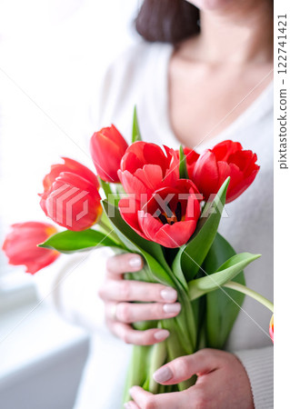 International Womens Day.Close-up of a woman in a white sweater with a bouquet of red tulips. 122741421
