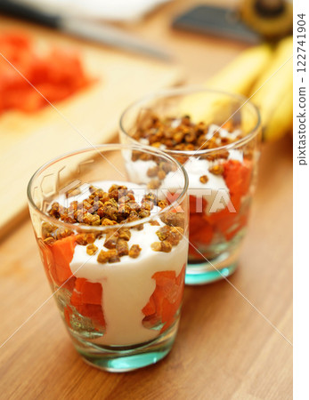 Two glasses of vegetarian yogurt dessert with papaya and granola on a wooden table 122741904