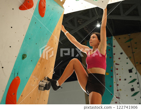 A strong female climber climbs an artificial wall with colorful grips 122741906