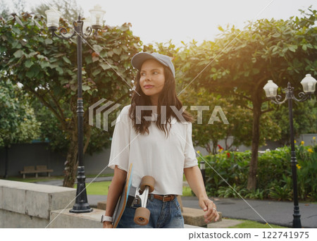 A woman is walking at the city park while carrying a skateboard in her hands 122741975