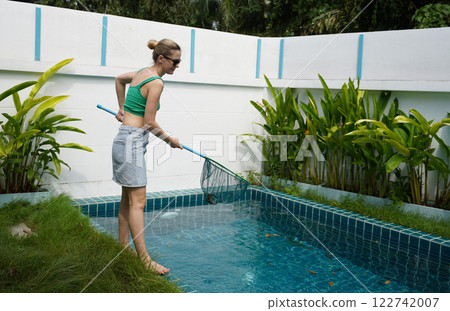 A young woman clean leaves out of a pool A young woman clean leaves out of a pool 122742007