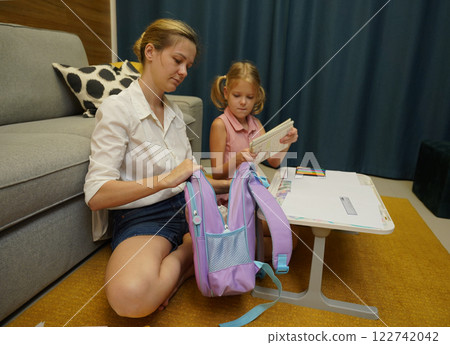 Mother helps her daughter pack her backpack Mother helps her daughter pack her backpack 122742042