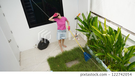 A woman raking the lawn at the backyard of her house  122742054