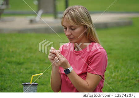 Young woman beading colorful bracelets outdoors in a park Young woman beading colorful bracelets outdoors in a park 122742075