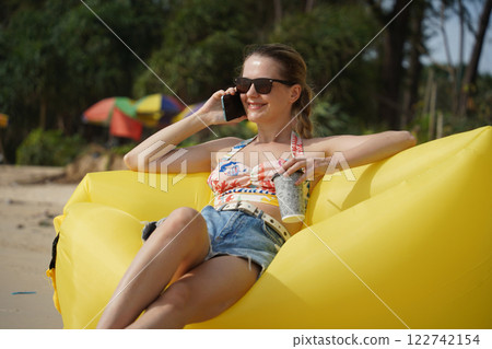 A young woman on the beach lounging on a yellow bean bag A young woman on the beach lounging on a yellow bean bag 122742154