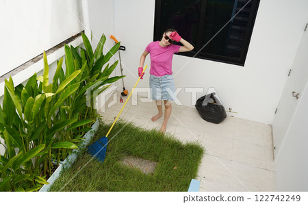 A woman raking the lawn at the backyard of her house  122742249