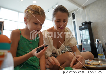 Mother and her daughter paint Halloween cookies  122742250
