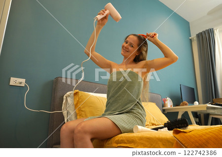 A woman is expertly styling her hair using a blow dryer and brush while in the bathroom 122742386