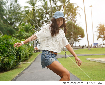 A young woman is skillfully riding a skateboard down a scenic park A young woman is skillfully riding a skateboard down a scenic park 122742567