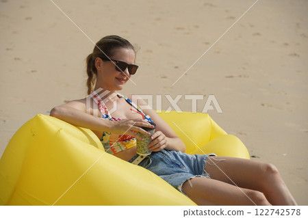 A young woman on the beach lounging on a yellow bean bag A young woman on the beach lounging on a yellow bean bag 122742578