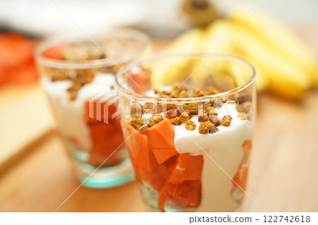 Two glasses of vegetarian yogurt dessert with papaya and granola on a wooden table 122742618