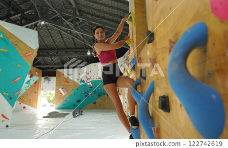 A strong female climber climbs an artificial wall with colorful grips 122742619